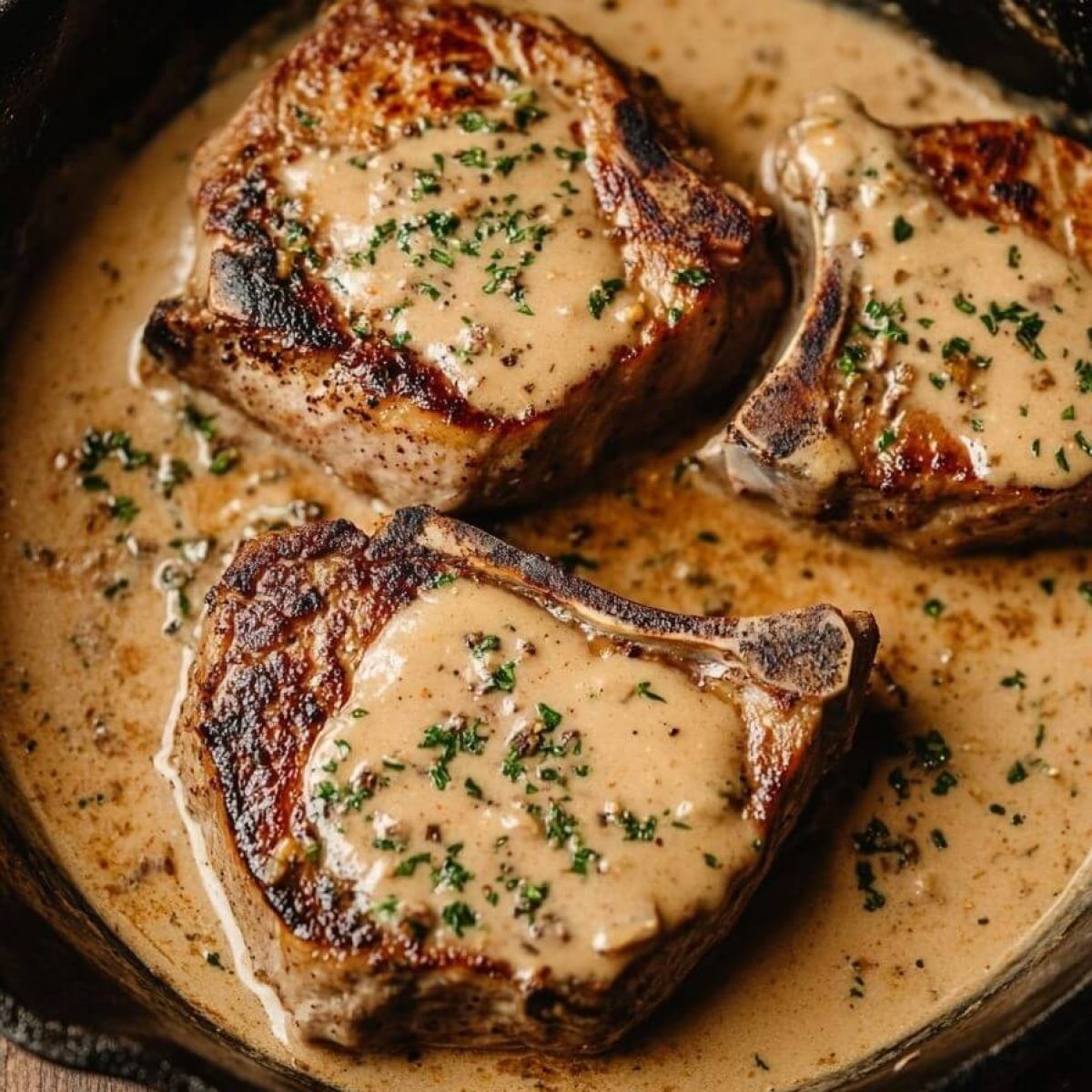 Three bone-in smothered pork chops in creamy gravy in a cast-iron skillet