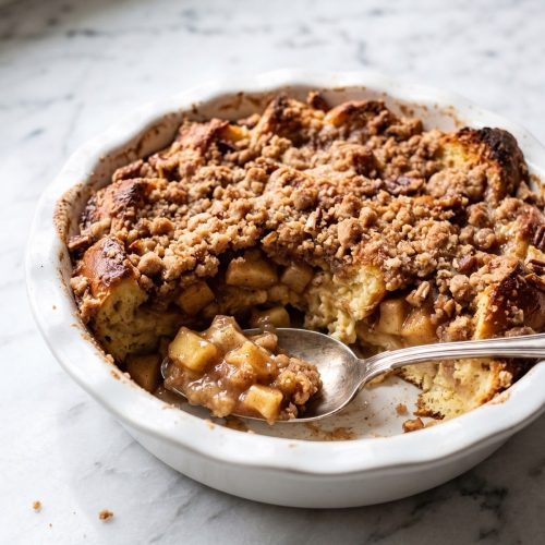 Golden apple pie French toast casserole scooped to show the apple and custard-soaked bread layers.
