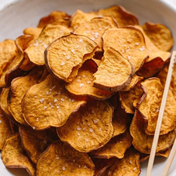 A white bowl piled high with crisp, golden baked sweet potato chips sprinkled with kosher salt