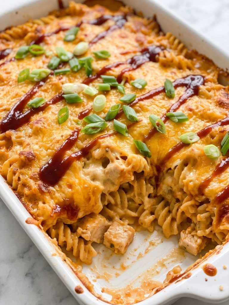 BBQ chicken pasta casserole with melted cheddar and a barbecue sauce drizzle in a baking dish