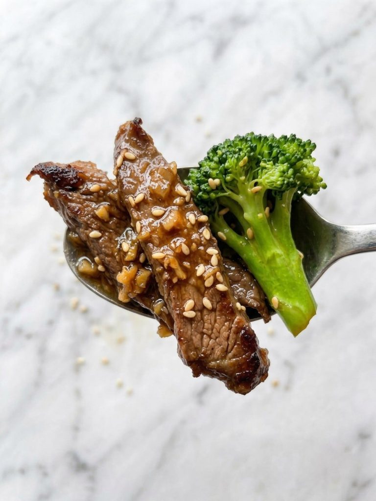 Close view of seared flank steak strips and broccoli in glossy teriyaki sauce with sesame seeds