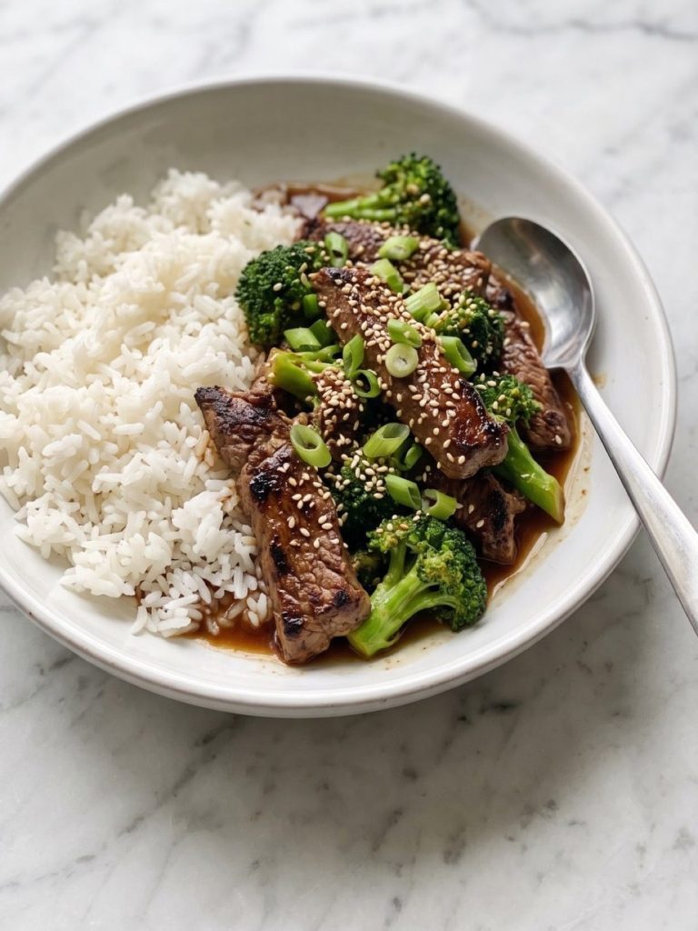 Beef and broccoli teriyaki over white rice in a wide bowl, topped with sesame seeds
