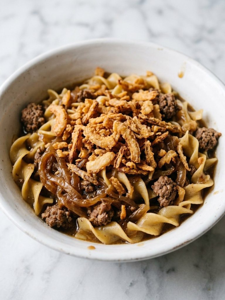 Close view of a bowl of egg noodles with ground beef, caramelized onions and crispy fried onions