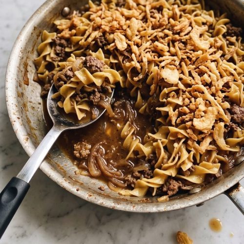 Beef French onion soup casserole with egg noodles and crispy fried onions in a skillet, with a serving scooped out