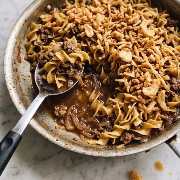 Beef French onion soup casserole with egg noodles and crispy fried onions in a skillet, with a serving scooped out