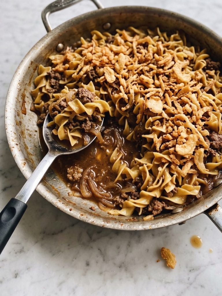 Beef French onion soup casserole with egg noodles and crispy fried onions in a skillet, with a serving scooped out