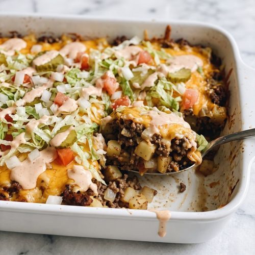 Scoop of potato and ground beef casserole with melted cheddar, burger sauce, lettuce, tomato, onion and pickle chips