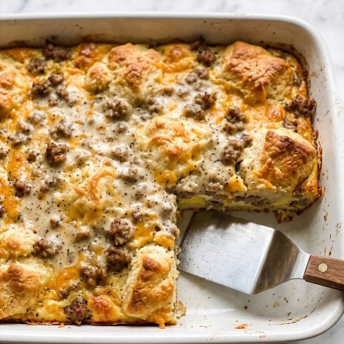 A baking dish of biscuits and gravy casserole with golden puffed biscuits and sausage gravy