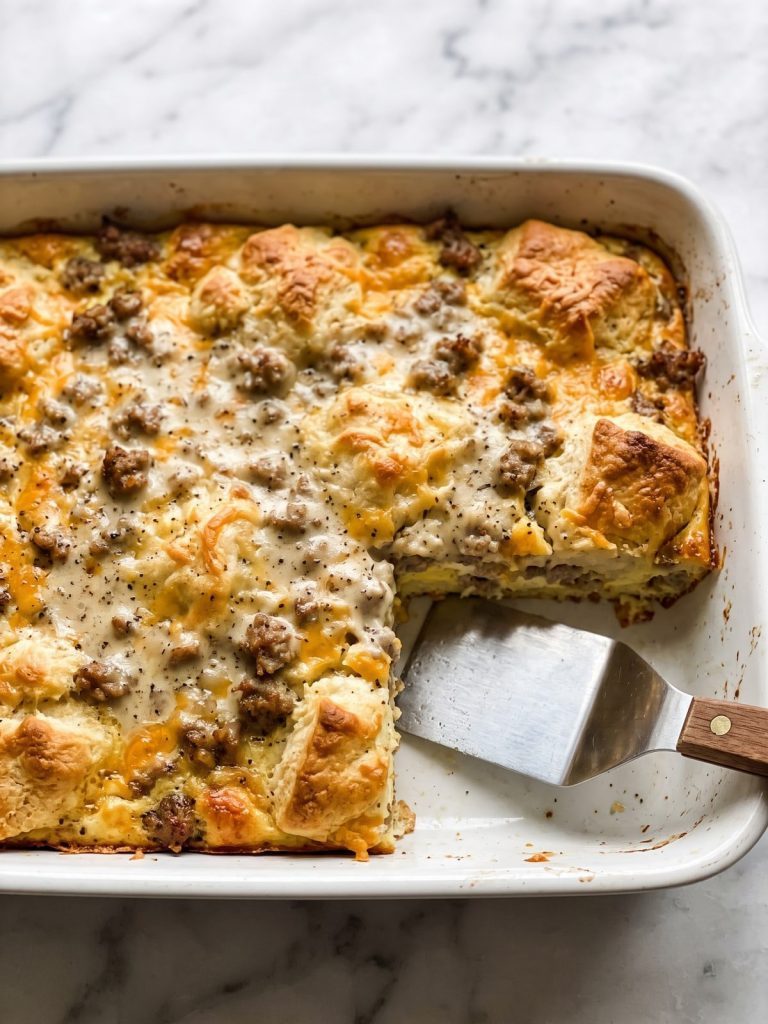 A baking dish of biscuits and gravy casserole with golden puffed biscuits and sausage gravy