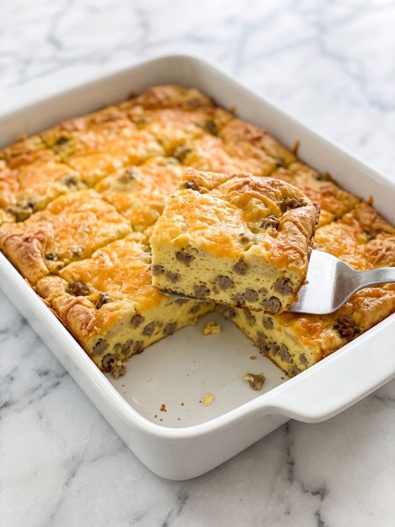Golden Bisquick sausage breakfast casserole in a white 9x13 baking dish with one square lifted out