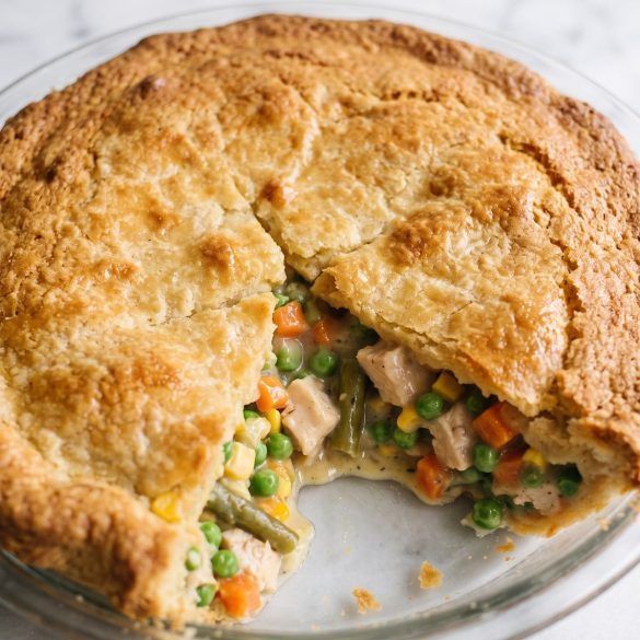 Chicken pot pie with a golden baked batter crust in a glass pie pan, one slice removed