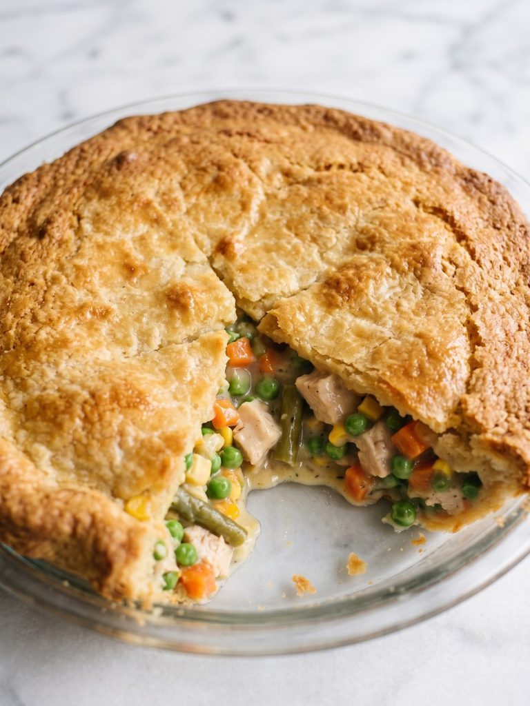 Chicken pot pie with a golden baked batter crust in a glass pie pan, one slice removed