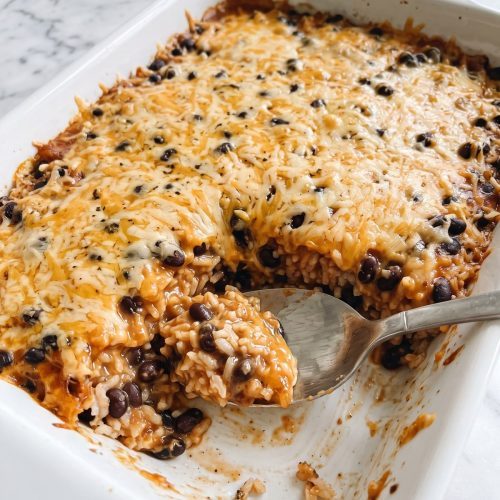 A baking dish of black bean rice casserole with melted cheddar on top, one serving scooped out to show black beans and rice in a red salsa sauce