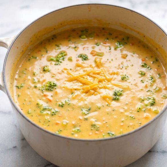 A Dutch oven of smooth golden cheesy broccoli soup with small broccoli florets and flecks of carrot
