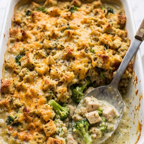 Chicken broccoli stuffing casserole in a white baking dish with a golden stuffing and cheese top, one serving scooped out