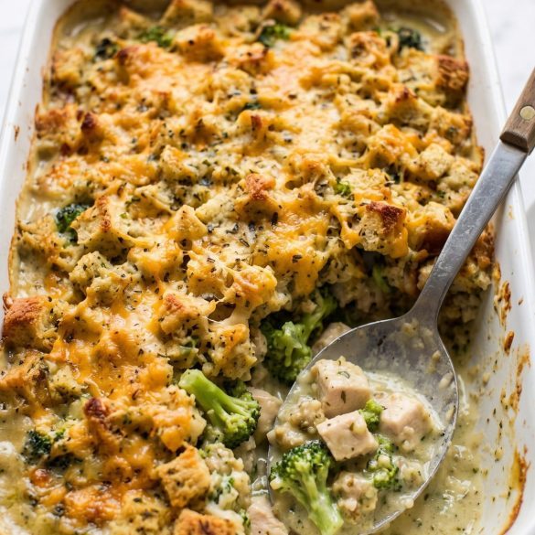 Chicken broccoli stuffing casserole in a white baking dish with a golden stuffing and cheese top, one serving scooped out