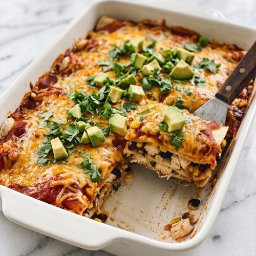 A baking dish of layered chicken enchilada casserole with melted cheese and cilantro