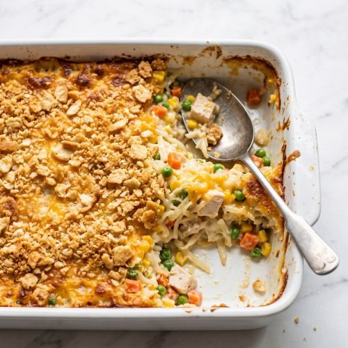 A baked chicken hashbrown casserole with a golden cracker topping in a white baking dish, one corner scooped out