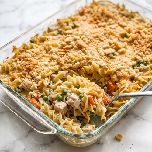 Chicken noodle casserole scooped from a glass baking dish, showing creamy noodles, chicken, vegetables and golden cracker crumbs
