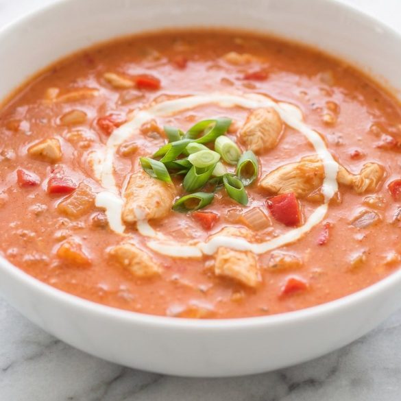 A bowl of creamy paprika-red chicken soup with a swirl of sour cream and green onion