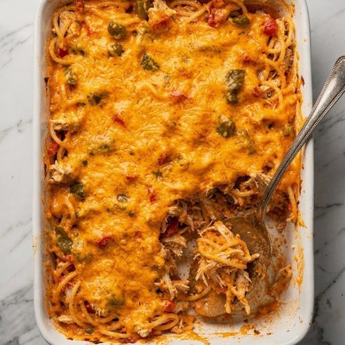 Cheesy chicken Rotel spaghetti casserole in a white 9x13 dish with a serving lifted out