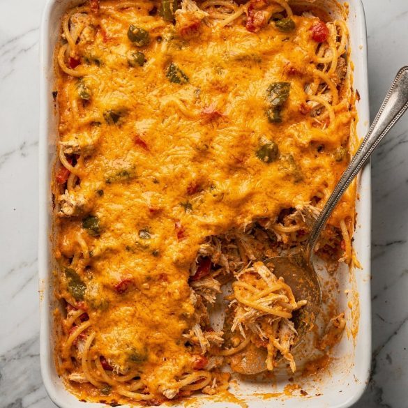Cheesy chicken Rotel spaghetti casserole in a white 9x13 dish with a serving lifted out