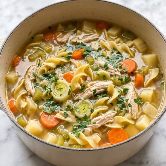A pot of chicken noodle soup with shredded drumstick meat, carrots, potatoes and egg noodles
