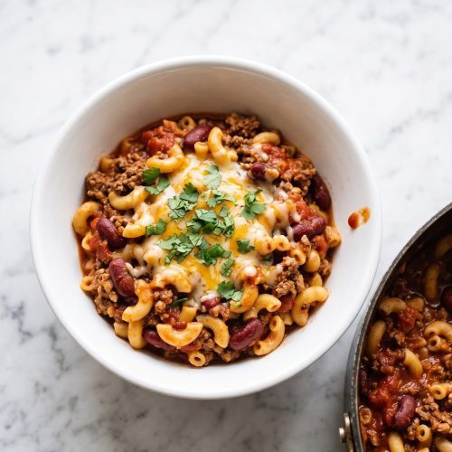 A bowl of chili mac scooped from a pot, showing beef, beans, elbow macaroni and melted cheese