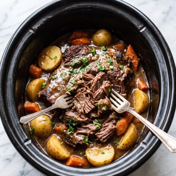 A slow cooker of tender shredded chuck roast with baby potatoes and carrots in a glossy brown gravy