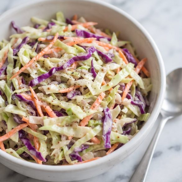 A white bowl filled with creamy coleslaw of green cabbage, purple cabbage and shredded carrot