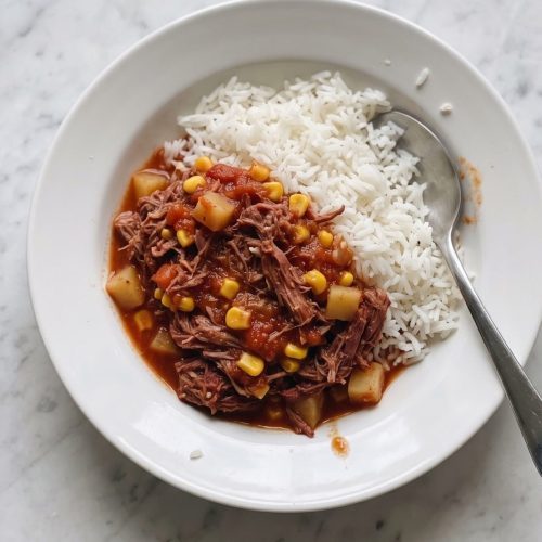Saucy corned beef with potatoes and corn over white rice in a shallow bowl