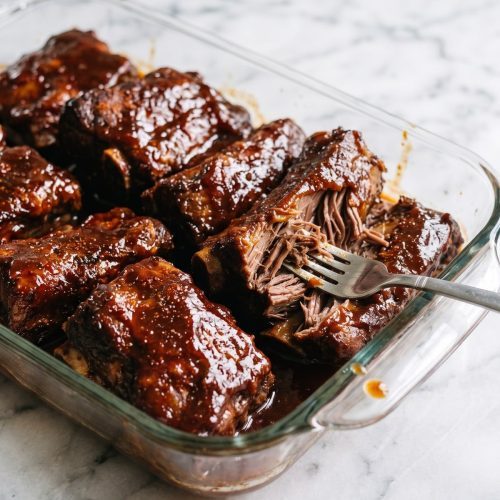Sauced country-style beef ribs in a baking dish with one rib pulled apart to show the tender meat.
