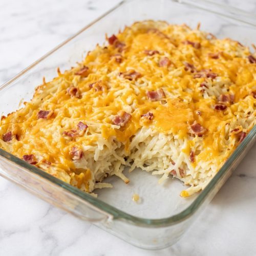 Golden cheesy bacon-ranch hash brown casserole with a scoop removed to show the creamy potatoes inside