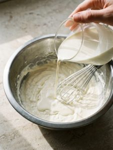 Cold heavy cream being poured into a smooth cream cheese mixture