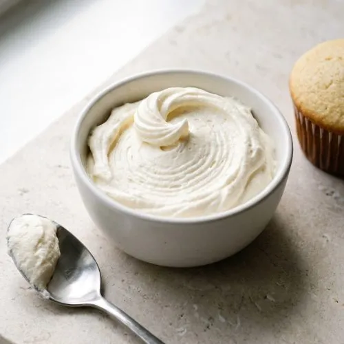 Cream cheese whipped cream in a white bowl with a spoonful beside it