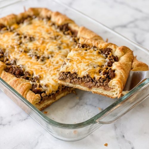 A sliced crescent roll taco bake showing its beef, bean, cheese, and crescent dough layers.