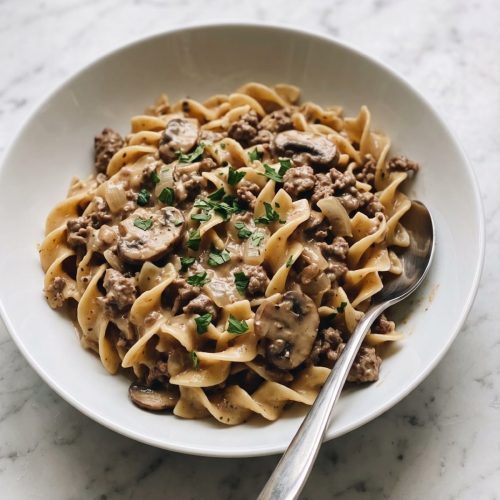 Ground beef stroganoff with egg noodles in a wide white bowl, creamy mushroom sauce and parsley