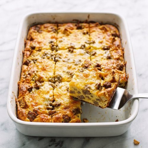Golden sausage and crouton egg bake in a white 9x13 dish with one square lifted out