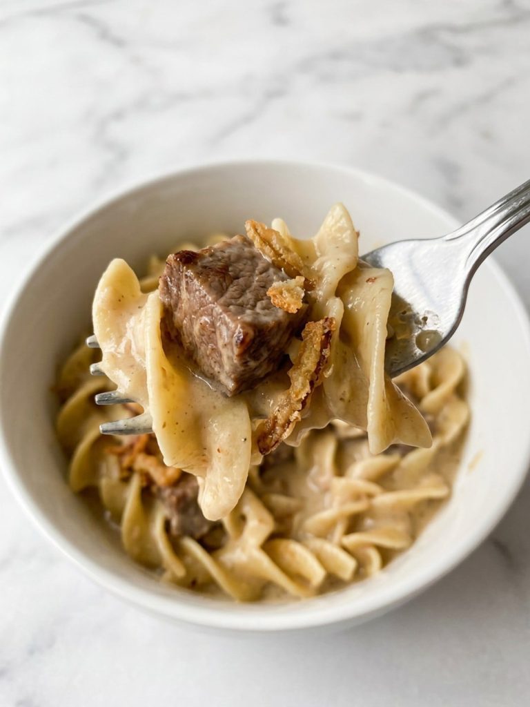 Close view of a forkful of egg noodles and a tender beef cube in creamy French onion sauce