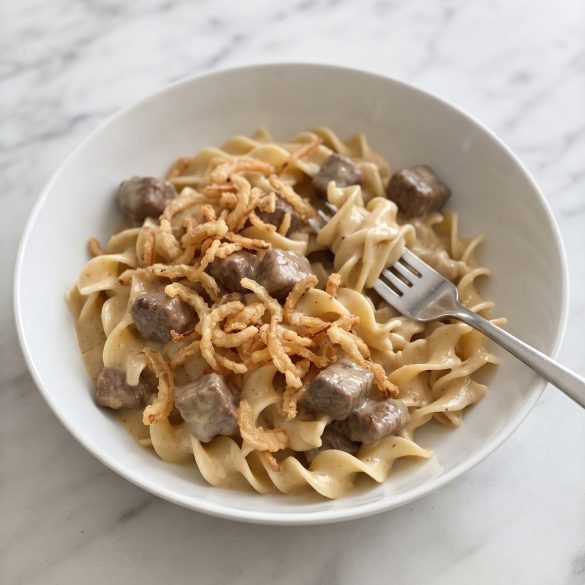 A bowl of creamy French onion beef and noodles with tender beef cubes, topped with crispy fried onions