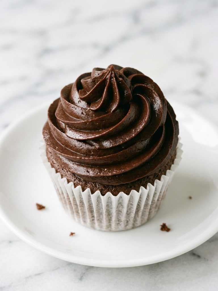 Close view of a chocolate cupcake topped with a tall swirl of fudge frosting