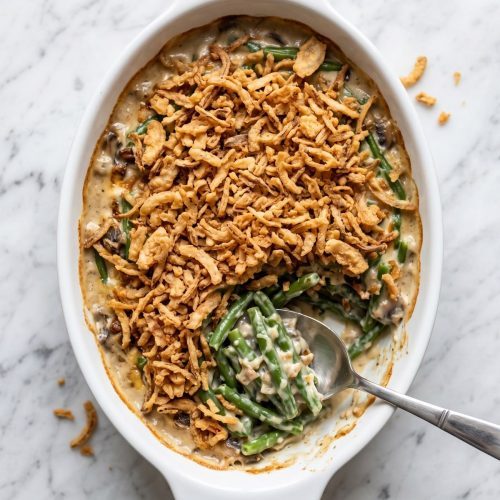 Green bean casserole with crispy fried onions in a white baking dish, with a serving scooped out