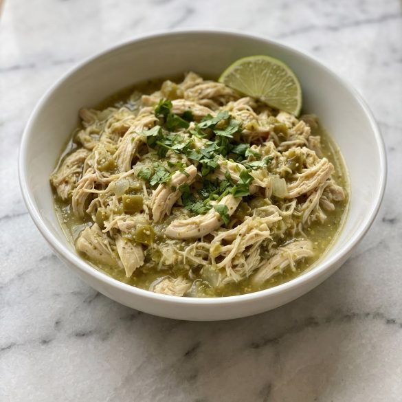 Shredded green chile chicken in salsa verde in a bowl with cilantro and lime