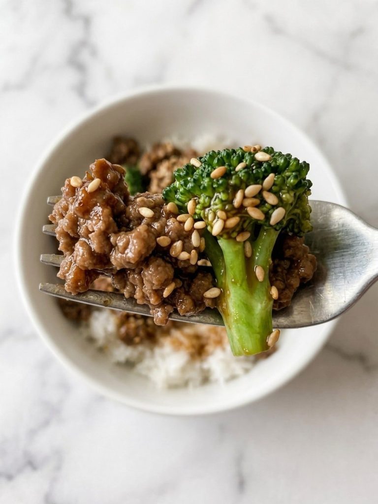 Close view of a forkful of browned ground beef and a broccoli floret in glossy sauce over rice