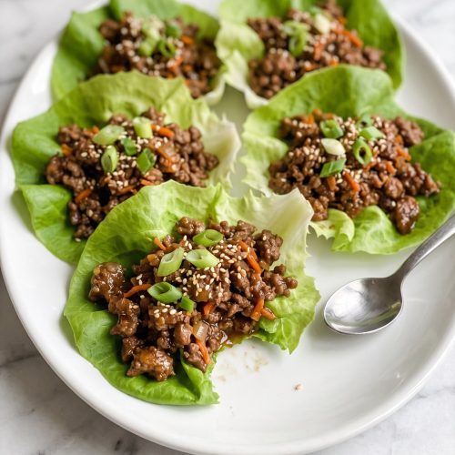 Butter lettuce cups filled with saucy ground beef, carrots, green onions and sesame seeds on a white platter