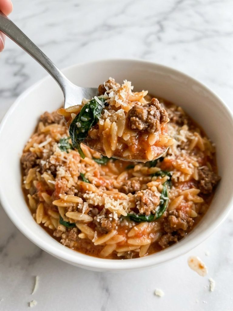 Close view of a spoonful of creamy tomato orzo with ground beef and spinach