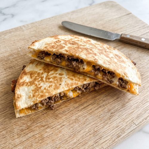 Golden ground beef quesadillas cut in half on a wooden board, showing seasoned beef and melted cheese inside