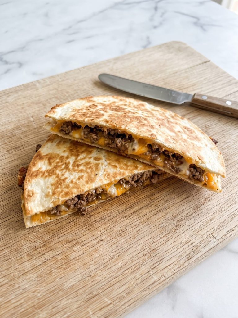 Golden ground beef quesadillas cut in half on a wooden board, showing seasoned beef and melted cheese inside