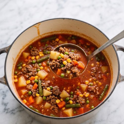 Pot of ground beef soup with potatoes and mixed vegetables, with a ladle lifting a scoop