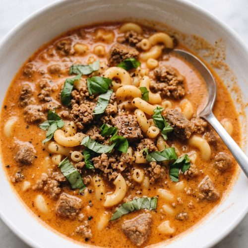 A bowl of creamy tomato soup with ground beef and elbow macaroni topped with fresh basil